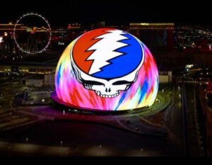 “Dead & Company performing at the Sphere in Las Vegas, surrounded by immersive psychedelic visuals and a vibrant audience, highlighting the venue’s cutting-edge technology and the band’s iconic energy.”