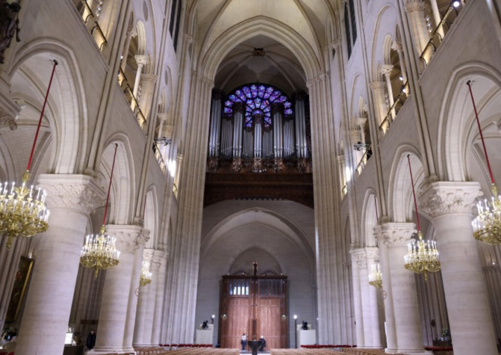 Alt Text: Ongoing reconstruction of Notre Dame Cathedral as seen from the New York Times coverage, showing scaffolding enveloping the iconic Gothic structure, workers restoring intricate stone carvings, and the rebuilding of the spire using traditional craftsmanship and modern engineering techniques.