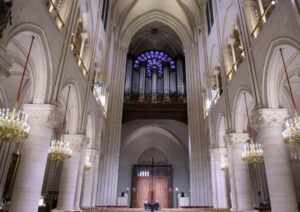 Alt Text: Ongoing reconstruction of Notre Dame Cathedral as seen from the New York Times coverage, showing scaffolding enveloping the iconic Gothic structure, workers restoring intricate stone carvings, and the rebuilding of the spire using traditional craftsmanship and modern engineering techniques.