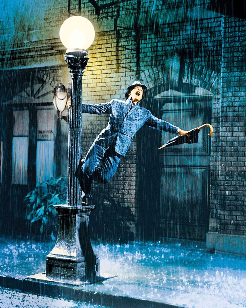 Gene Kelly performing “Singin’ in the Rain,” dancing joyfully in the iconic rain-soaked scene from the 1952 musical