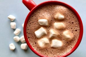 A steaming mug of holiday hot chocolate topped marshmallows, and festive sprinkles on a cozy winter table.