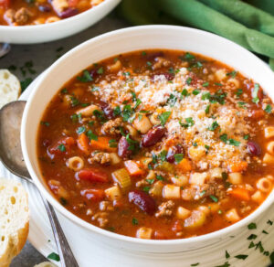 A steaming bowl of traditional Pasta Fagioli with small pasta, beans, and a rich tomato broth, garnished with parsley and Parmesan