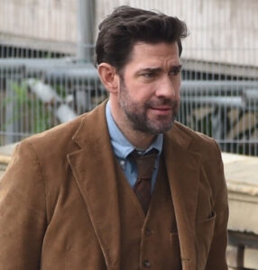 John Krasinski in rugged adventurer attire, exploring ancient ruins in the first-look image from Guy Ritchie’s Fountain of Youth