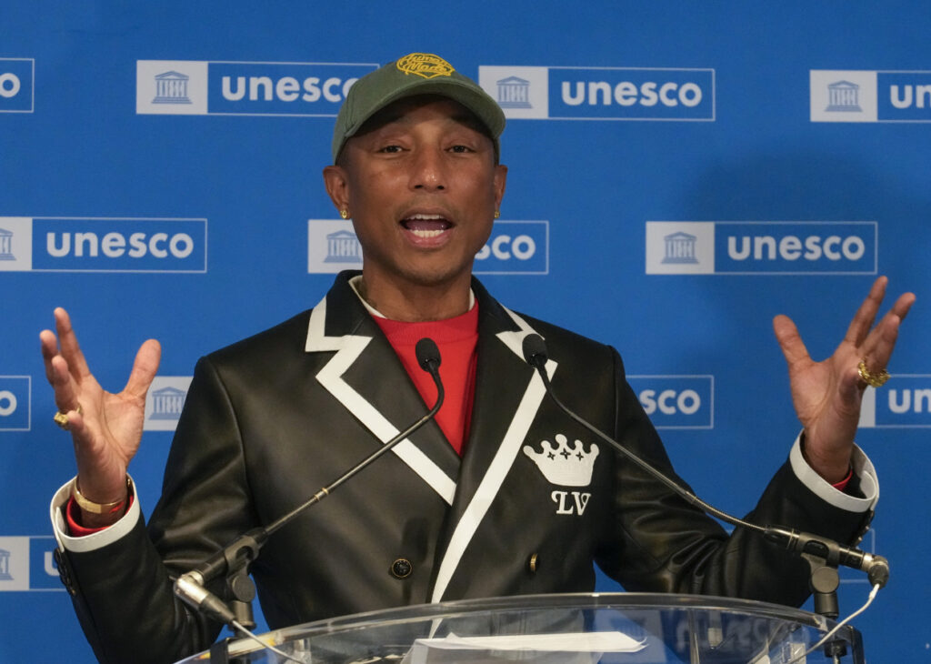 Pharrell Williams smiling at a UNESCO event, wearing a tailored suit, symbolizing his role as a Goodwill Ambassador