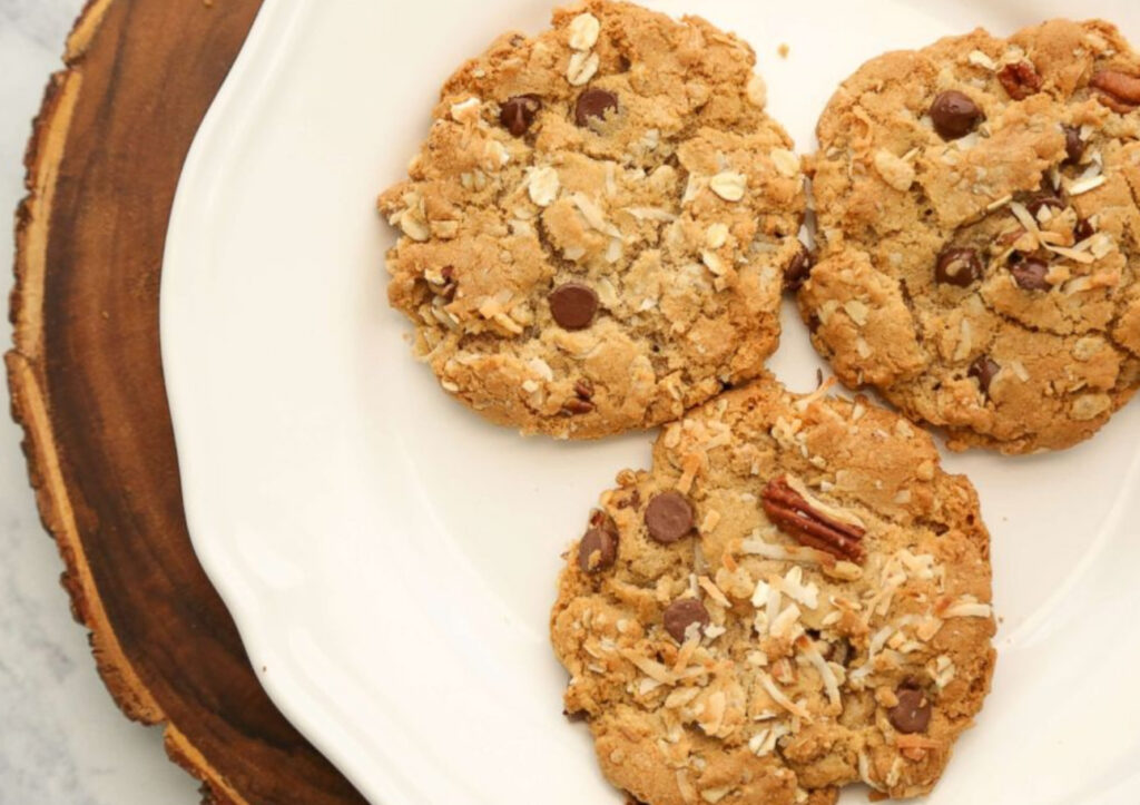 A plate of Reese Witherspoon’s Cowboy Cookies featuring oats, chocolate chips, pecans, and coconut flakes on a rustic wooden table