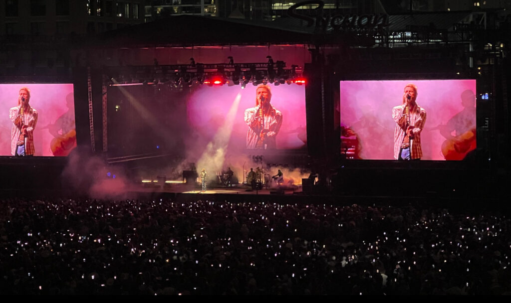 Post Malone performing onstage at the Wild Horses Festival 2025, engaging with a massive crowd under vibrant stage lighting