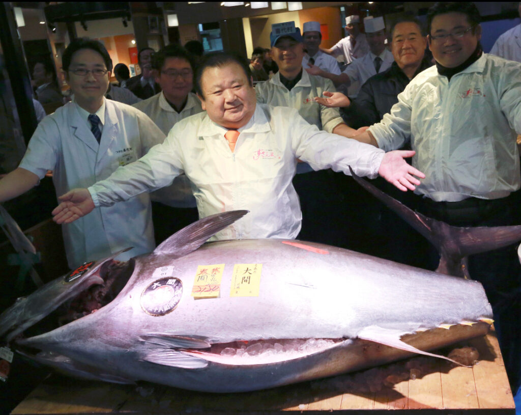 Alt Text: A record-breaking 608-pound bluefin tuna on display at Tokyo’s fish market auction, surrounded by buyers and sellers