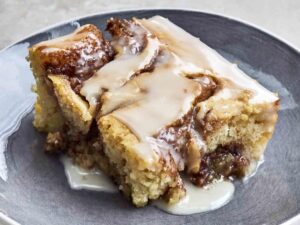 A slice of Big Mama’s Cinnamon Roll Poke Cake topped with a rich cinnamon-brown sugar filling and buttery icing