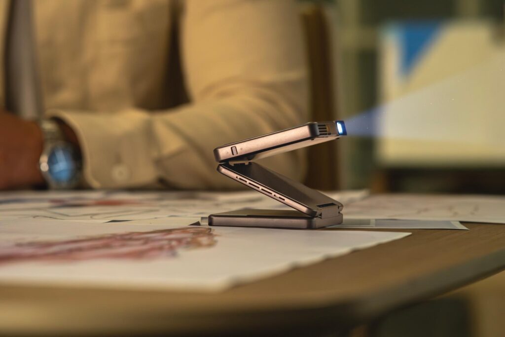 Aurzen Zip pico projector with a tri-fold Z-shaped stand, compact design, and vibrant projection on a portable device