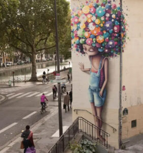 A mural by Vinie featuring her iconic female character with graffiti-inspired hair blending seamlessly into its surroundings