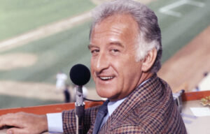 Bob Uecker at a Milwaukee Brewers game, holding a microphone with his iconic smile, symbolizing his legacy in baseball