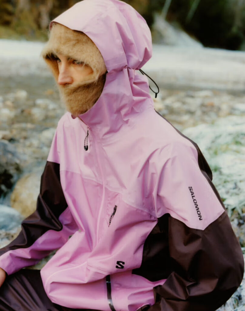 A model wearing Salomon’s Spring/Summer 2025 Slate Collection, featuring a sleek shell jacket and trail-ready pants on a rocky trail