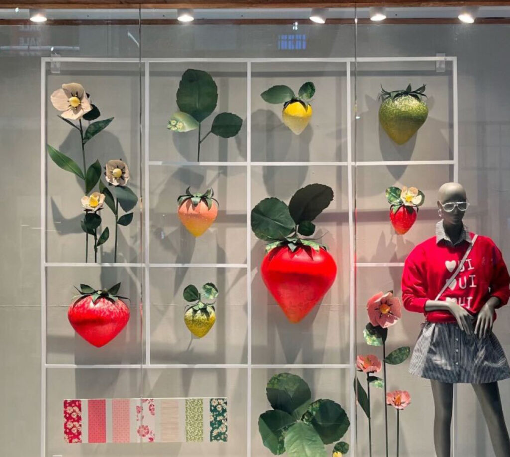 Anthropologie’s vibrant strawberry-themed window display featuring oversized fruit props and spring-inspired decor