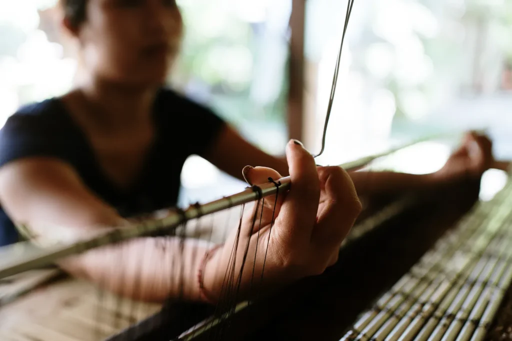 A traditional Indonesian weaver working on a loom, creating intricate patterns using natural dyes and heritage techniques