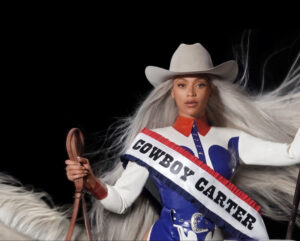 Beyoncé poses in Western-inspired attire, announcing the Cowboy Carter Tour 2025 with a neon-lit desert sign