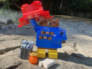 A detailed LEGO Paddington Bear figure, wearing his classic blue coat and red hat, holding a suitcase and marmalade sandwich