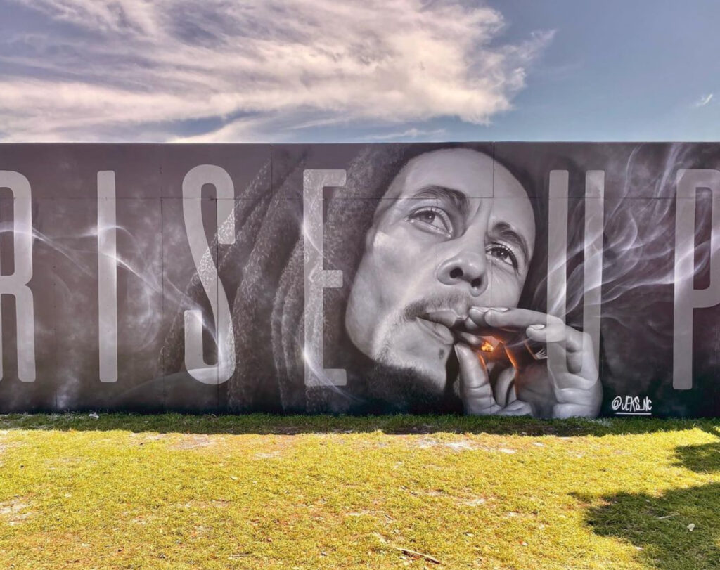 JEKS ONE’s hyperrealistic mural of a woman with a red rose covering her eye and a golden halo around her head