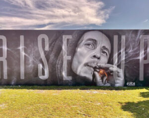 JEKS ONE’s hyperrealistic mural of a woman with a red rose covering her eye and a golden halo around her head