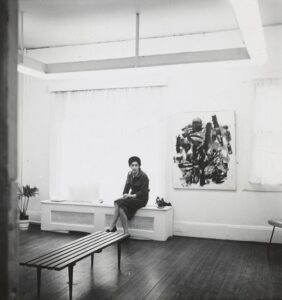 Michael Corinne West standing beside her painting Vietnam Summer (1963), showcasing her bold Abstract Expressionist style