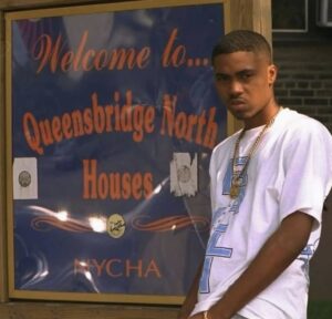 Nas in 1996 posing in front of the Queensbridge North Houses sign, representing his upbringing and influence on hip-hop