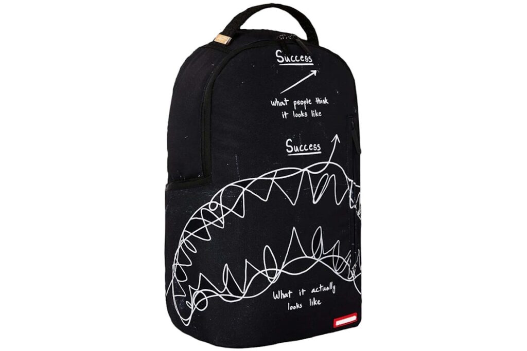 A Sprayground Success Scribble Shark DLXSR Backpack featuring a bold shark mouth design with a graffiti-inspired scribble pattern