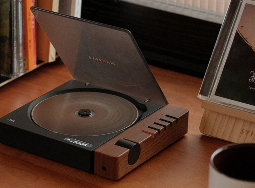 Sleek modern CD player with vertical disc slot, designed by Shenyang Judian Design Co., Ltd, on a minimalist wooden shelf