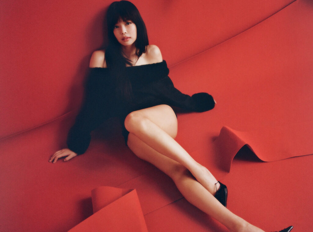 Jennie Kim poses in theatrical red lighting to promote her debut solo album Ruby, symbolizing transformation and bold artistry
