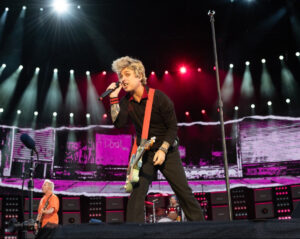 Green Day performing live on stage with Billie Joe Armstrong mid-scream during a high-energy punk rock set
