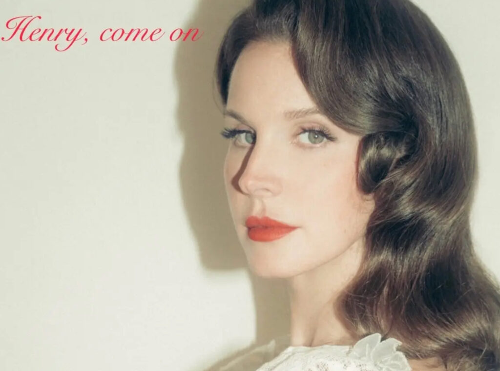 Lana Del Rey in a prairie dress standing in a sunlit field, evoking the country-inspired mood of her single “Henry, come on.”