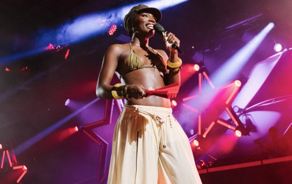Doechii performing onstage at H&M&LA 2025 festival in downtown Los Angeles with neon lights and cheering crowd