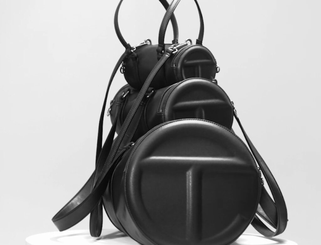 Large Telfar Duffle bag in black vegan leather with embossed TC logo, shown on a model in casual urban streetwear