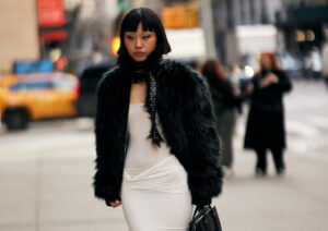 Model in oversized faux fur coat and furry hat walking down a city street, embodying 2025 fashion trends
