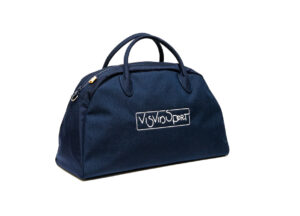 The VISVIM SPORT Boston bag made of canvas and leather rests on a wooden bench, evoking vintage athletic travel aesthetics