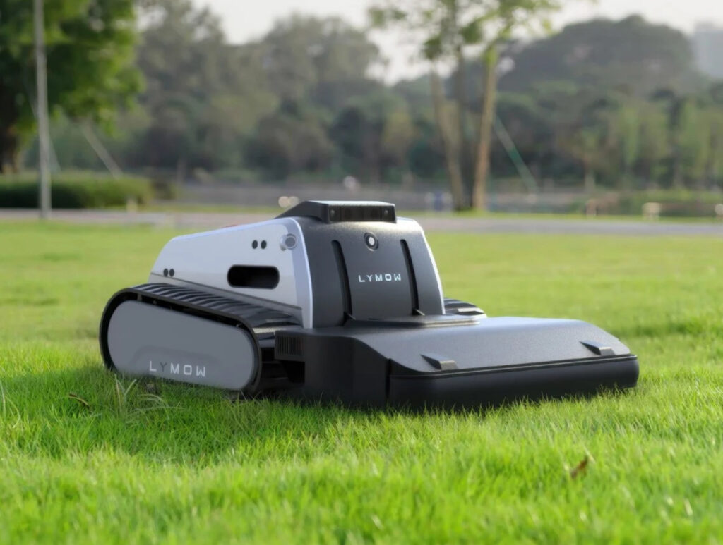Lymow One autonomous lawn mower on a green lawn, featuring sleek design, treaded tires, and dual-blade cutting system