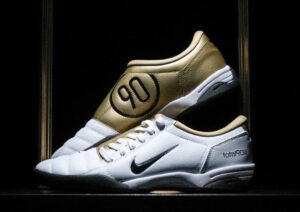 Side view of the Nike Total 90 White Gold Unisex Shoe, showcasing the iconic 90 logo and metallic gold detailing