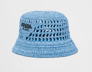 A woman wearing Miuccia Prada’s signature Re-Nylon bucket hat, styled for casual elegance and sun protection