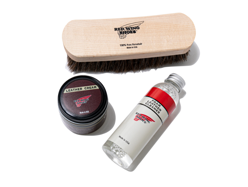 Red Wing shoe care kit featuring a horsehair brush, leather cream, and foam cleaner arranged beside classic leather boots