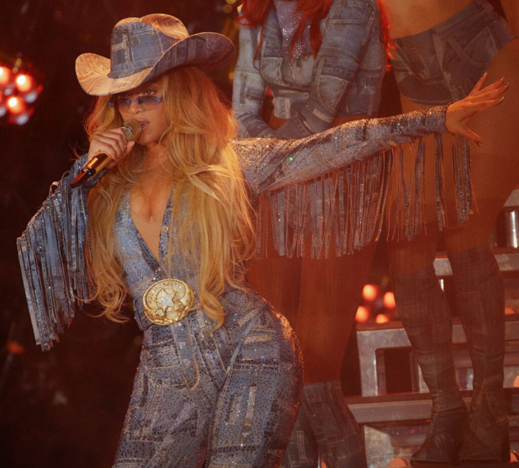 Beyoncé performing at SoFi Stadium in a custom Roberto Cavalli crystal-fringed denim-print outfit and cowboy hat