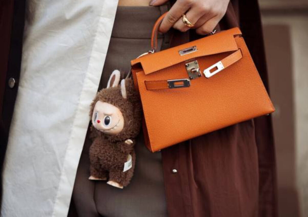 A Labubu doll clipped to a luxury designer handbag at Paris Fashion Week, worn by a model in street-style fashion