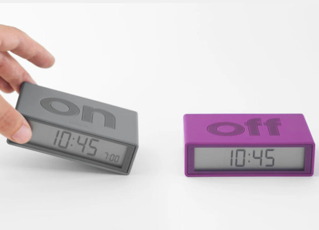 Flip Alarm Clock by DesignWright showing “ON” “OFF” side up, with minimalist block design and bold type on a bedside table