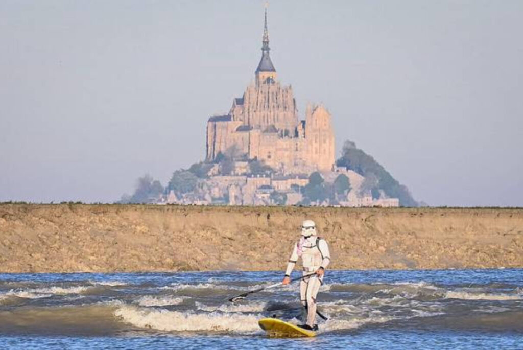 Stormtrooper paddleboards across Mont Saint-Michel Bay in France, combining Star Wars cosplay with historic coastal scenery