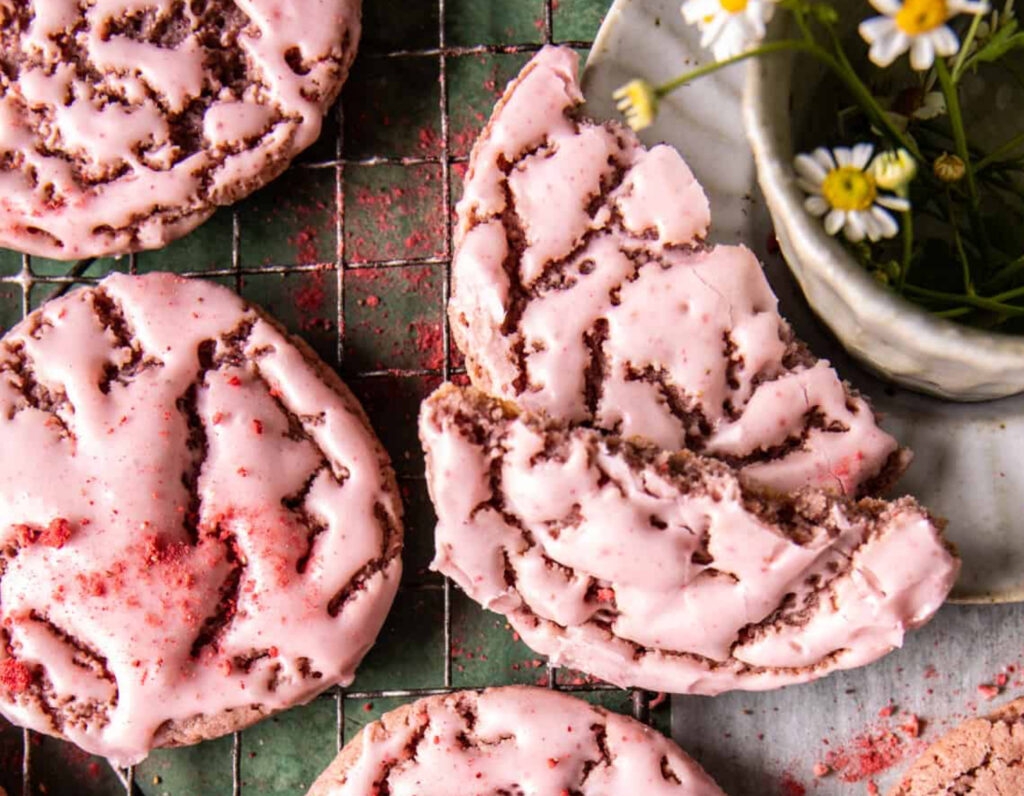 A stack of soft, pink strawberry sugar cookies topped with strawberry cream cheese icing, displayed on a cooling rack