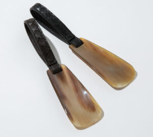 Bottega Veneta haute shoe horn displayed on a leather bench beside polished dress shoes
