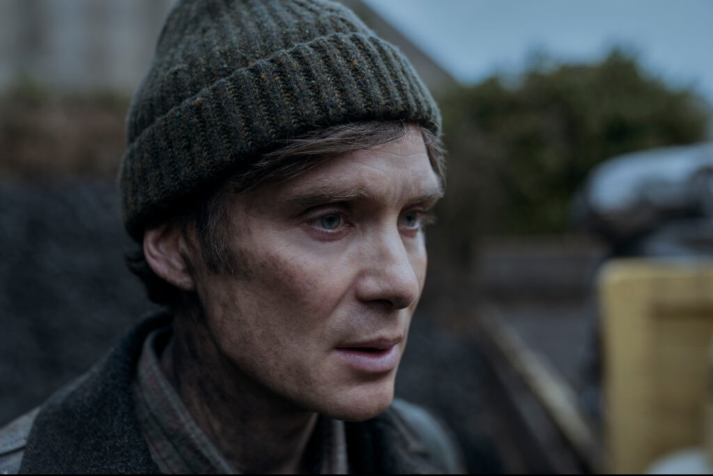 Cillian Murphy as Bill Furlong in Small Things Like These, standing solemnly in front of a foggy Irish village