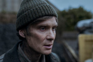 Cillian Murphy as Bill Furlong in Small Things Like These, standing solemnly in front of a foggy Irish village