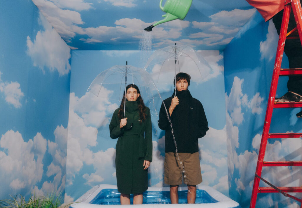 Model wearing Holzweiler Pre-Fall 2025 sun-faded oversized shirt and terry popover hoodie on a Norwegian coastline