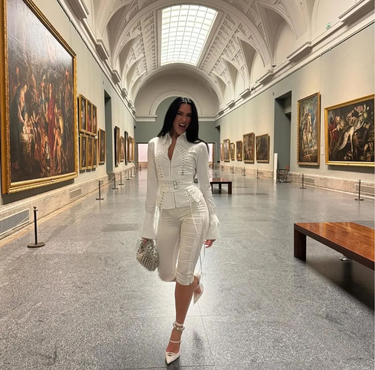 Dua Lipa poses in a historic museum hall wearing a Dilara Findikoglu ensemble, surrounded by classical sculptures and art