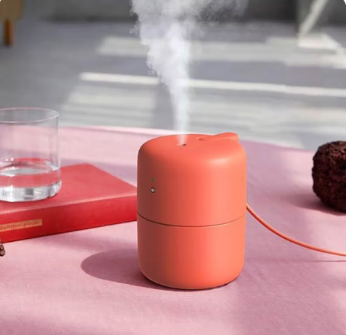 Minimal USB desktop humidifier emitting mist on a modern wooden desk setup