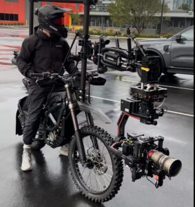 Lucas Tomoana in black riding gear on an electric dirt bike fitted with a stabilized camera rig for dynamic film shooting