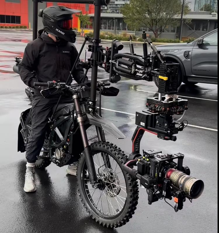 Lucas Tomoana in black riding gear on an electric dirt bike fitted with a stabilized camera rig for dynamic film shooting